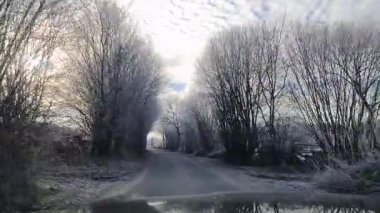 Kışın güneşli bir havada dar bir kırsal yolda hareket halindeki bir arabadan manzara.