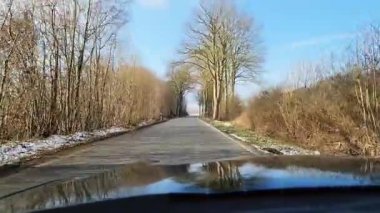 Kışın güneşli bir havada dar bir kırsal yolda hareket halindeki bir arabadan manzara.