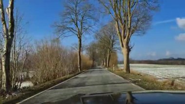 Kışın güneşli bir havada dar bir kırsal yolda hareket halindeki bir arabadan manzara.