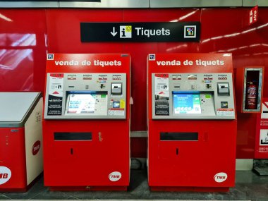 Barselona, 18 yaşında. Temmuz 2024: Barselona metro istasyonunda bekleyen iki adet kırmızı TMB bilet otomatı, bilet çıkarmaya hazır