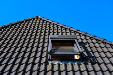 Açık çatı penceresi eğimli bir çatıda açık mavi gökyüzüne karşı doğal ışık ve havalandırma sağlıyor.