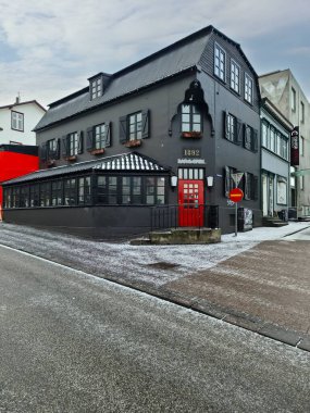 Reykjavik, İzlanda - 05. Mart 2025: İzlanda 'nın Reykjavik kentinde sokakta kırmızı kapı ve kar bulunan geleneksel siyah İzlanda evi