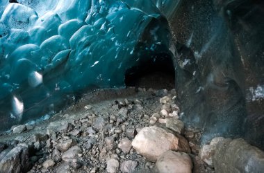 Kayalar ve çakıllar, vatnajokull buzulu, İzlanda 'daki bir buz mağarasında, parlak mavi bir buz tavanının altındaki karanlık bir açıklığa açılıyor.