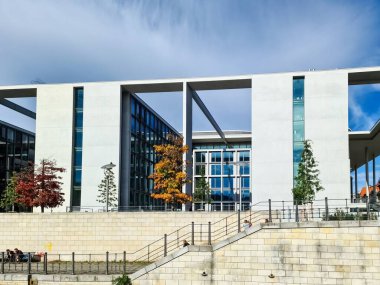 Berlin, Almanya 03. Ekim 2024 'te, Berlin, Almanya' da berrak bir mavi gökyüzü altında canlı sonbahar ağaçları arasında yükselen modern beyaz bina çarpıcı bir kentsel manzara yarattı.