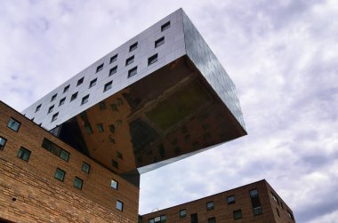 Berlin, Almanya 03. Ekim 2024, Berlin, Almanya 'da bulutlu bir gökyüzünün altında tuğla binaların üzerinde kantiver bir yapıya sahip modern cam ve çelik bina