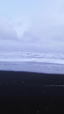 Reynisfjara 'nın karanlık volkanik kıyı şeridine vuran güçlü dalgalar karamsar bulutlu gökyüzünün altındaki dramatik kıyı manzarasını gözler önüne seriyor.