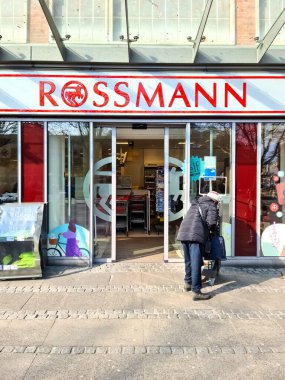 Kiel, Almanya, 12 Mart 2025, Almanya 'da güneşli bir kış gününde Rossmann eczanesinden alışveriş arabasıyla ayrılan son sınıf öğrencisi.