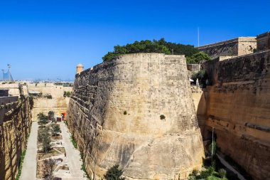Valletta, Malta 27. Eylül 2024, Malta 'daki Valletta tahkimatlarında açık mavi gökyüzünün altında iki büyük duvarı ayıran kuru bir hendek.
