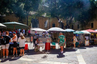 Valletta, Malta 27. Eylül 2024, turistler güneşli bir günde güneşli bir günde güneşli bir günde Valletta, Malta 'nın şehir merkezindeki açık hava pazarından hediyelik eşya alıyorlar.