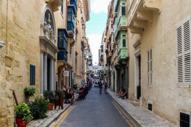 Valletta, Malta 27. Eylül 2024, insanlar Valletta, Malta 'da güneşli bir günde renkli balkonları ve açık hava kafeleri olan tipik bir caddede eğleniyorlar.
