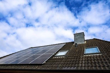 Fotovoltaik paneller, bulutlu bir gökyüzü altında sürdürülebilir enerji üretimi için güneş enerjisini kullanan fayanslı bir çatıya kurulur.