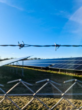 Dikenli teller ve tel örgüler açık mavi gökyüzünün altındaki bir güneş enerjisi santralini koruyor.