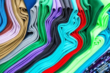 Katlanmış renkli kıyafetler, canlı ve çeşitli kumaşlar içeren dalgalı bir desen oluşturuyor.