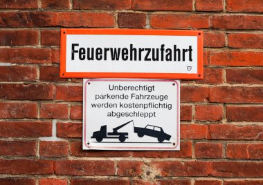 Kiel, Almanya 15 Mart 2025, Kiel, Almanya 'daki tuğla duvarda iki tabela, itfaiye girişini gösteriyor ve izinsiz park cezasının çekici ile sonuçlanacağı uyarısı var.