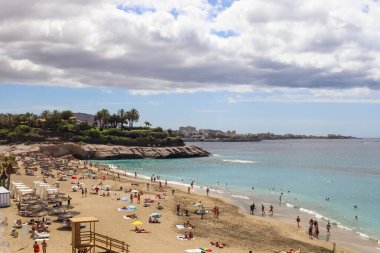 Turistler Tenerife, Kanarya Adaları 'ndaki kalabalık bir plajda yaz tatilinin tadını çıkarıyorlar.