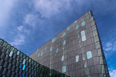 Harpa Konser Salonu 'nun modern geometrik cephesi Reykjavik, İzlanda' daki mavi gökyüzünü ve bulutları yansıtıyor.