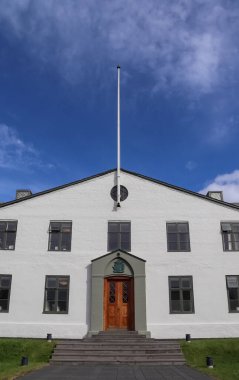 Reykjavik, İzlanda 'da mavi gökyüzünün altında bulunan ahşap kapı ve bayrak direğiyle beyaz boyanmış hükümet binası.