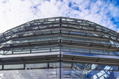 Reichstag 'ın modern cam kubbesi Berlin, Almanya' daki mavi gökyüzünü ve bulutları yansıtıyor.