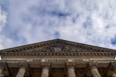 Reichstag binasının ön cephesine Alman Halkı için Dem Deutschen Volke yazısıyla alçak açılı bir bakış açısı ve Almanya, Berlin 'de bulutlu bir gökyüzü.