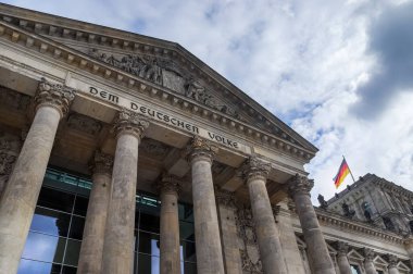Düşük açı, Berlin 'de bulutlu bir gökyüzüne karşı Alman bayrağıyla süslenmiş Reichstag binasının etkileyici görünüşünü yansıtıyor.