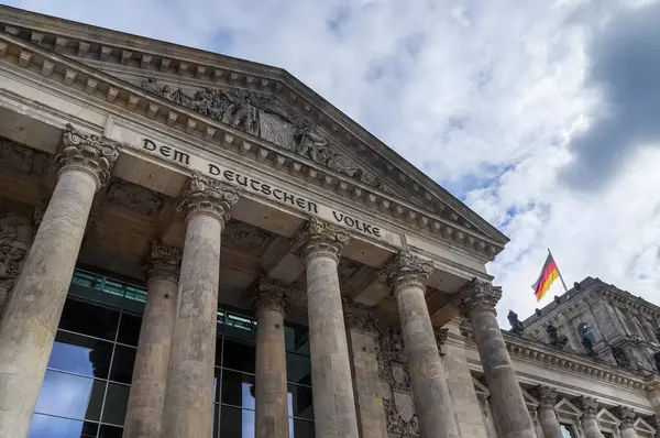 Düşük açı, Berlin 'de bulutlu bir gökyüzüne karşı Alman bayrağıyla süslenmiş Reichstag binasının etkileyici görünüşünü yansıtıyor.