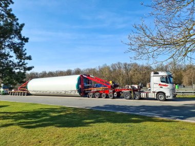 Hamburg, Almanya - 28. Mart 2024: Özel bir römorkta büyük bir rüzgar türbini taşıyan kamyon, ormanlık bir alana yakın bir yolda ilerliyor