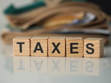 Dört tahta küp yazım vergisi istiflenmiş belgelerin bulanık arka planına sahip yansıtıcı bir yüzeye oturur.