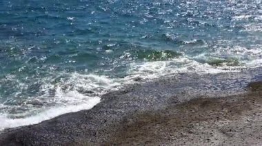 Sakin dalgalar yavaşça karanlık volkanik kayaların üzerinden geçiyor Tenerife kıyı şeridi boyunca, güneş ışığı barışçıl Atlantik Okyanusu kıyı şeridini aydınlatıyor