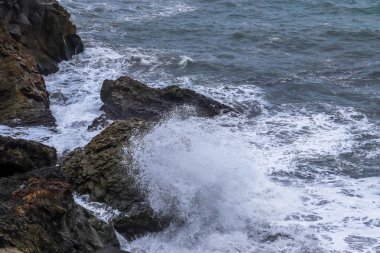 Güçlü okyanus dalgaları İzlanda kıyılarında kayalara çarpıp beyaz köpük ve sprey oluşturur.
