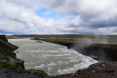 Gullfoss şelalesinin İzlanda 'daki Hvt nehrine akışı dramatik bulutlu bir gökyüzü altında sisli bir atmosfer yaratıyor. 