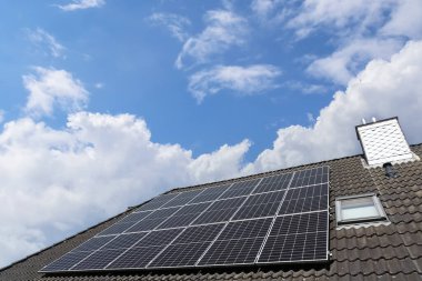 Fotovoltaik paneller, bulutlarla benekli parlak bir gökyüzü altında sürdürülebilir enerji üretimi için güneş enerjisini kullanan bir çatıya kurulur.