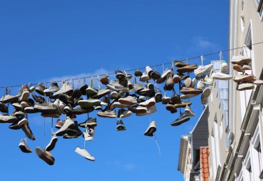 Birçok spor ayakkabısı Almanya 'nın Flensburg şehrinin merkezindeki bir kabloda asılı duruyor ve arka planda açık mavi bir gökyüzü var.