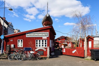 Kırmızı ahşap evler ve güneşli bir bahar gününde park etmiş bisikletlerle çevrili Flensburg Müzesi 'nin çatısını dekore eden ters dönmüş bir tekne.