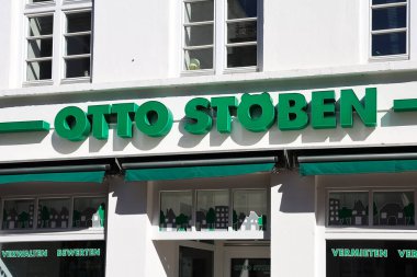 Flensburg, Almanya 'da beyaz bir binanın ön cephesinde yeşil Otto Stoben logosu kiralama, yönetme ve mülkiyet değerlendirmesi gibi emlak hizmetleri sunuyor.