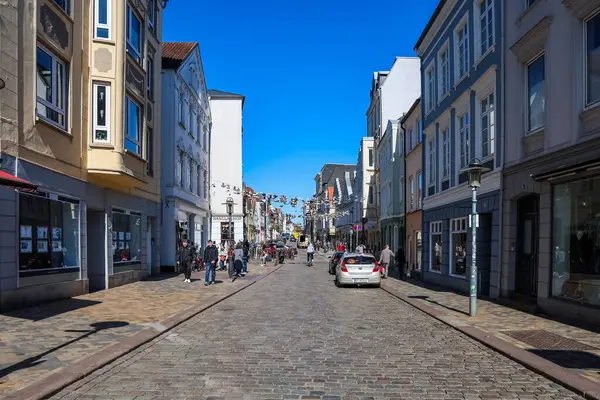 Yayalar ve bisikletçiler, Almanya 'nın Flensburg kentindeki Grosse Caddesi' nde güneşli bir günün tadını çıkarıyorlar.