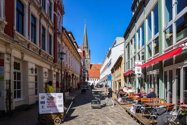 Açık kafeler, sokak satıcıları ve renkli binaların üzerinde yükselen Aziz Nikolai Kilisesi 'nin çan kulesi Almanya' nın Flensburg şehrinde bir yaya sokağı oluşturuyordu.