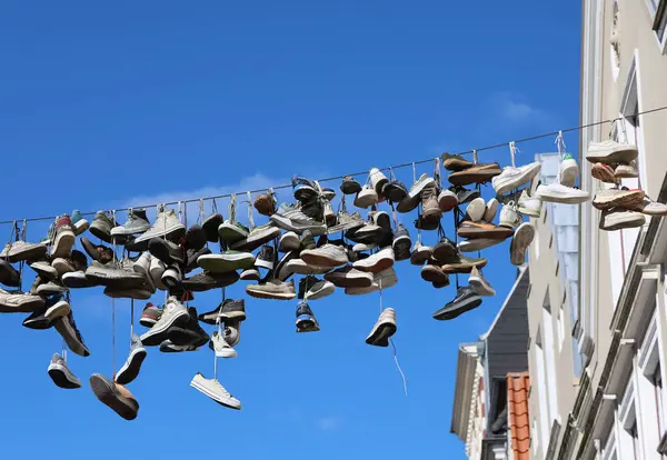 Birçok spor ayakkabısı Almanya 'nın Flensburg şehrinin merkezindeki bir kabloda asılı duruyor ve arka planda açık mavi bir gökyüzü var.