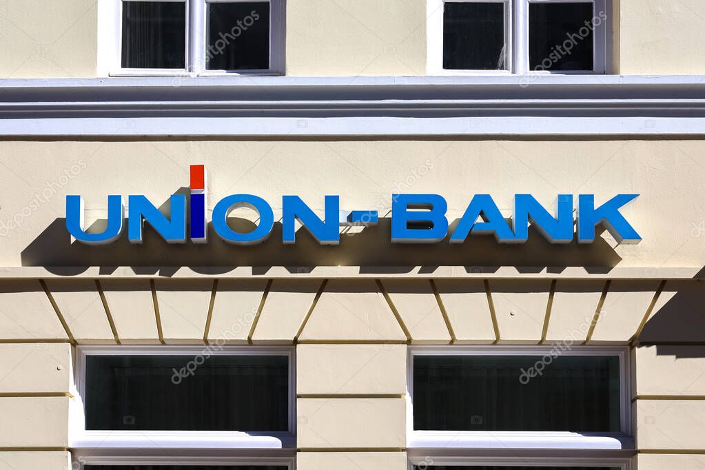 Blue and red Union Bank logo is mounted on a beige building facade with windows, reflecting sunlight on a bright day in Flensburg, Germany