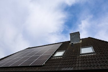 Çatıya bacası ve tavan penceresi olan fotovoltaik paneller kurulmuş. Bulutlu bir gökyüzü altında temiz enerji sağlıyor.