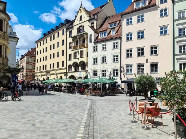 Münih, Almanya - 22. Haziran 2024: Münih, Almanya 'da renkli tarihi binalarla çevrili bir kaldırım taşı meydanında yürüyen ve dinlenen insanlar