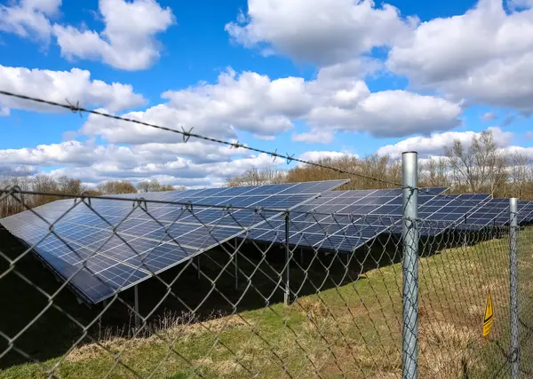 Fotovoltaik paneller, bulutlu mavi gökyüzünün altında dikenli tellerin arkasında yenilenebilir enerji üretiyor.