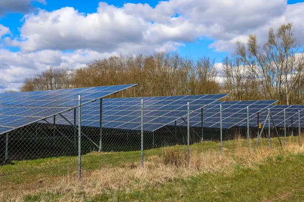 Fotovoltaik paneller metal bir çitin arkasında güneş ışığını yakalıyor ve sürdürülebilir bir gelecek için yenilenebilir enerji üretiyor.