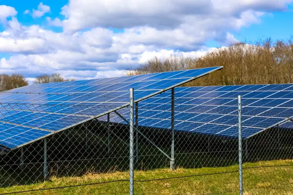 Güneş panellerinin sıraları tel örgülerin arkasında duruyor, parlak mavi gökyüzünün altında güneş ışığını elektriğe dönüştürüyorlar.