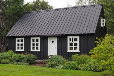 Seydisfjordur, İzlanda - 13. Haziran 2024: Seydisfjordur, İzlanda 'da beyaz pencereli ve bahçeli siyah boyalı ahşap ev, geleneksel mimariyi ön plana çıkarıyor