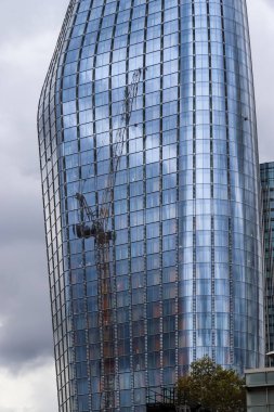 Londra, Birleşik Krallık - 04. Ekim 2024: Londra 'da arka planda bulutlu gökyüzü olan inşaat vincini yansıtan modern cam gökdelen
