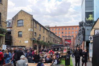 Londra, Birleşik Krallık - 04. Ekim 2024: Londra 'daki Camden Market' te yürüyen ve yemek yiyen insanlar, tuğla binalar ve bulutlu gökyüzüyle