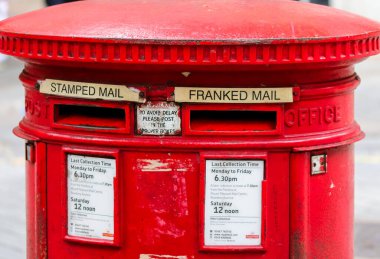 Londra, Birleşik Krallık - 04. Ekim 2024: Kırmızı Kraliyet Posta Kutusu, Londra caddesinde klasik İngiliz posta iletişimini somutlaştıran koleksiyon saatlerini ve posta depolarını gösteriyor