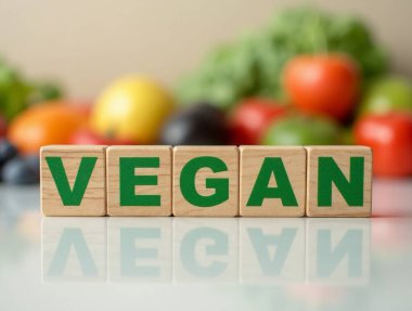 Arka planda bulanık meyve ve sebzelerle dolu ahşap mektup bloklarıyla yazılmış vegan sağlıklı bir yaşam tarzını teşvik ediyor.