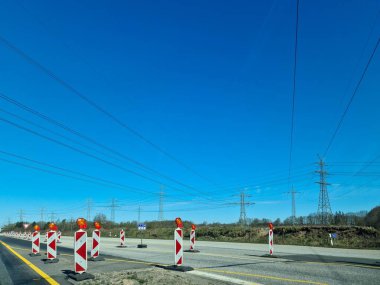 Kiel, Almanya - 19. Nisan 2025: Kırmızı ve beyaz çizgili trafik uyarı direkleri araçları mavi gökyüzünün altındaki bir yol inşaatına yönlendiriyor