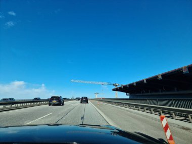 Kiel, Almanya - 19. Nisan 2025: Almanya 'da mavi gökyüzü arka planı üzerinde çalışan vinçle Kiel Kanal su yolu üzerinde inşaat halindeki otoyolda giden araçlar